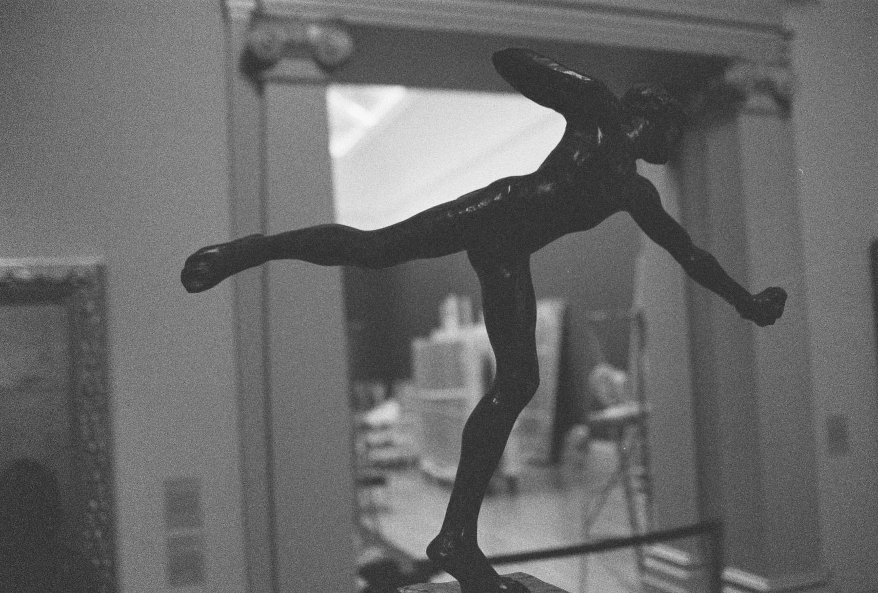 A bronze sculpture of a figure on one leg in a gallery